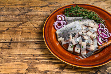 Pickled marinated herring fish sliced fillet on a plate with thyme and onion. wooden background. Top view. Copy space