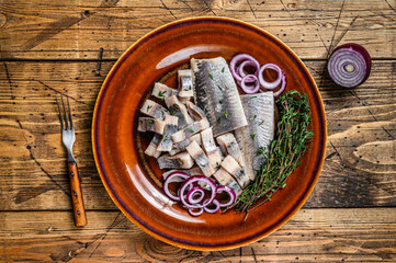 Obraz na płótnie Canvas Pickled marinated herring fish sliced fillet on a plate with thyme and onion. wooden background. Top view