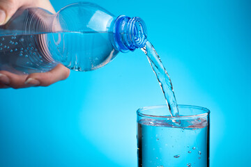 A woman pours water into a glass on a blue background. Side view, with space to copy. The concept of purified, mineral water.
