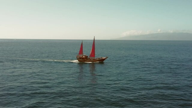 An old ship with crimson sails is sailing on the open ocean to meet adventures