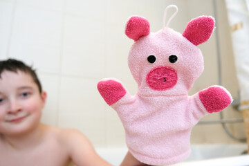 A boy in a bathroom showing funny piggy hand puppet toy washcloth close up, happy washing and shower concept