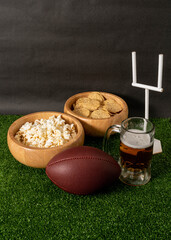 American football party. American football ball, beer, snacks and goal post on green grass and black background