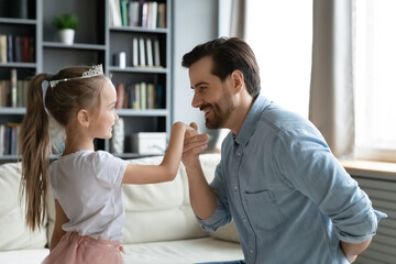Affectionate young dad kissing hand of cute 6s little kid daughter, practicing dancing waltz together at home. Caring millennial father pretending to be gentleman, playing with small girl as lady.