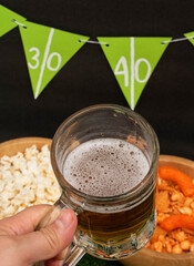 Woman hand holding a jar with beer. Snacks and banner on black background. American football decoration