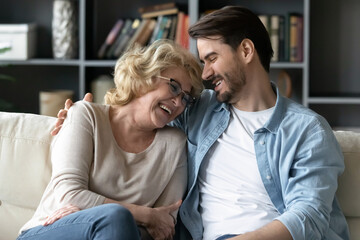 Happy older mature woman laughing at joke, communicating with grown son at home. Emotional different generations loving family having fun, discussing funny life moments, relaxing together on sofa.