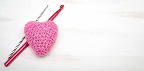 Crochet amigurumi - pink heart with crochet hooks on a white background. Valentine's day banner