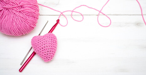 Knitted heart of pink thread with crochet hooks on a white background and a skein of thread for knitting. Valentine's Day.
