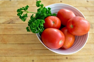 Bowl of fresh organic roma tomatoes from farmer's market displayed with green parsley ready for cooking or salad. Concept fresh, organic, healthy nutritional food, photo background