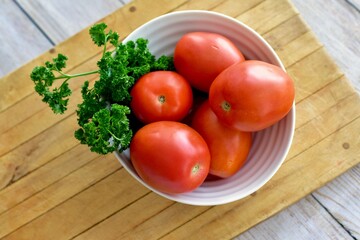 Bowl of fresh organic roma tomatoes from farmer's market displayed with green parsley ready for cooking or salad. Concept fresh, organic, healthy nutritional food, photo background