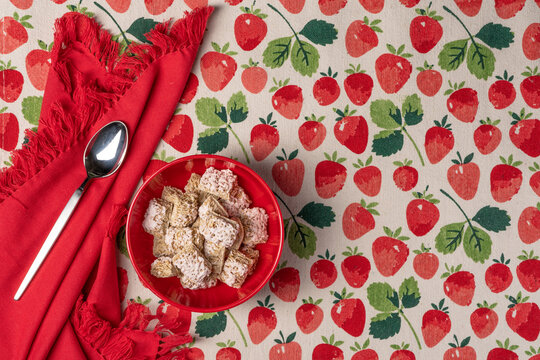 Spring Or Summer Breakfast Theme With Red Bowl Of Frosted Wheat Cereal,  Spoon And Napkin On A Strawberry Print Tablecloth