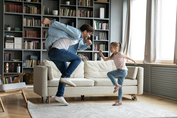 Crazy young happy energetic caucasian father having fun with adorable small 7s kid daughter, dancing to disco pop music together in living room, enjoying domestic active family pastime at home.