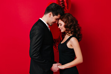 Romantic couple dancing in valentine's day. Studio photo of ginger girl holding hands with boyfriend on red background.