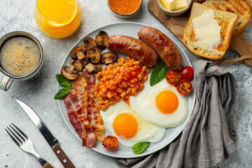 Full English breakfast on a plate with fried eggs, sausages, bacon, beans, toasts and coffee on light stone background. Top view