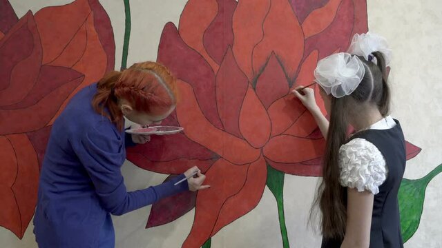 Two teenage girls paint a large red flower on the wall of a house with brushes. The concept. Close-up. 4K