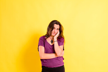 Young woman with anguished and uneasy expression, isolated on yellow studio background.