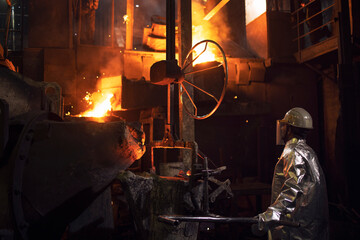 Hard work in foundry and melting iron in furnace. Workers controlling iron smelting in furnace.