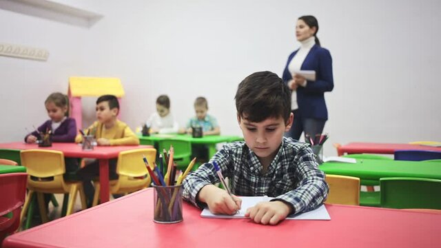 Portrait of little assiduous boy with pen and notebook at lesson in elementary school