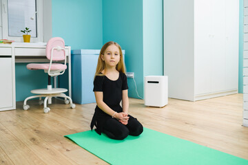 Small girl in black leotard sit on sport mat at home interior, workout training during...