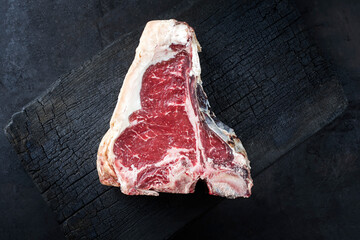 Raw dry aged wagyu t-bone beef steak offered as top view on a rustic charred wooden board with copy...