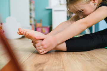 Close up small gymnast girl hands and feet during stretching workout on home floor at...