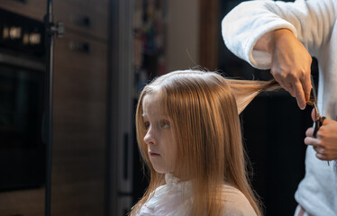 Fototapeta premium hair cutting at home, mom cuts daughter's hair in the kitchen
