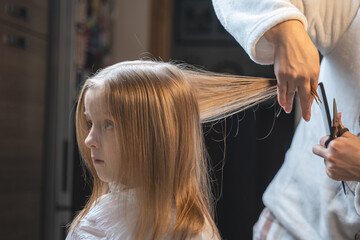 Fototapeta premium hair cutting at home, mom cuts daughter's hair in the kitchen