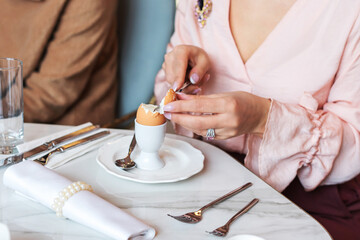 Fototapeta na wymiar A woman peels an egg for breakfast in a restaurant. Selective Focus
