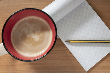 Mug of coffee, near to a notebook with a pencil, on th desktop.
