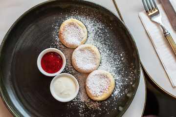 Dessert cottage cheese cakes with jam and sour cream on a dark plate