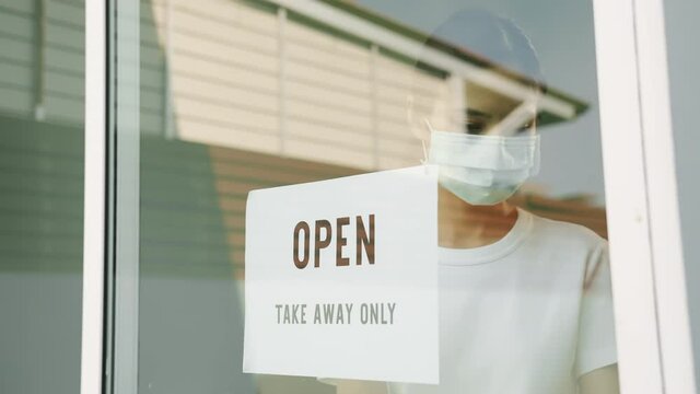 Young woman owner puts a OPEN take away only sign on the front door. Cafe or restaurant Affected by coronavirus disease.