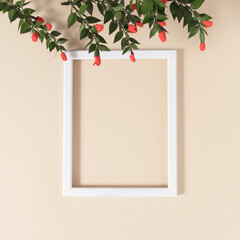 Creative copy space with white frame on sandy color background. Green branch with red berries. Modern design concept.