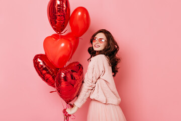 Studio shot of sensual ginger girl with red heart shaped balloons. Indoor photo of beautiful woman isolated on pink.