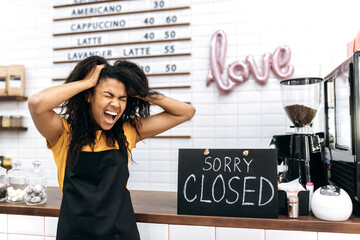 Emotional frustrated African American waitress, barista or small business owner in a black apron,...
