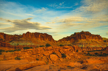 Sunset during golden hour in Southern Utah, sun warming red sandstone, cliffs, mountains, and mesa, and sun