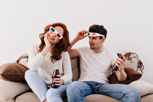 Couple watching 3d movie with interest. Smiling young people enjoying film and drinking soda.