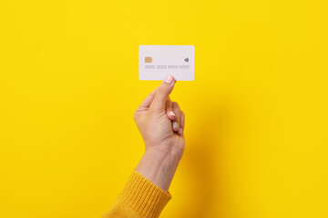 white credit card in female hand, card with electronic chip over yellow background