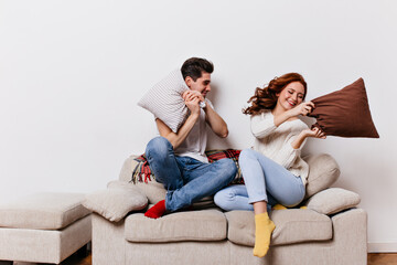 Fototapeta na wymiar Young people in jeans spending valentine's day at home. Smiling friends posing during pillow fight.