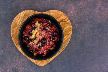 Serving of fresh baked blueberry strawberry crisp in a black bowl on a heart shaped wood board
