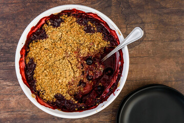 Fresh baked blueberry strawberry crisp baked in a white dish, sitting on a wood cutting board
