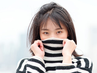 Close up portrait of young Chinese woman looking at camera with mouth covered by her sweater.