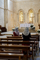 in una abbazia medievale ragazza col velo che prega , molto calda la luce delle finestre