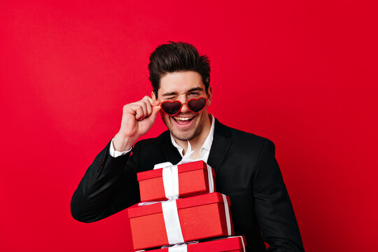 Confident man looking at camera through sunglasses. Studio shot of elegant boy with presents.