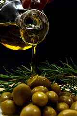 Glass bottle with virgin olive oil on a table with olives. Selective focus