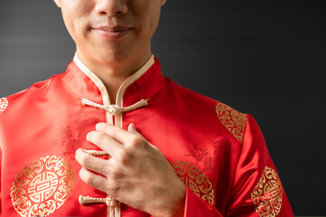 Portrait of happy positive young Asian business man in red Chinese clothes, Qipao or Cheongsam is smiling, touching clothes like suit with copy space to text with fade shade black background. - 409765806