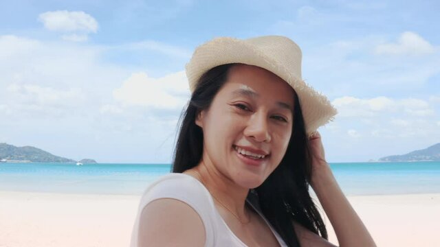 4K A happy carefree female tourist wear straw hat is making selfie or video call with phone to a friends or family on a desert offshore seaside in a sunny day during vacation trip.