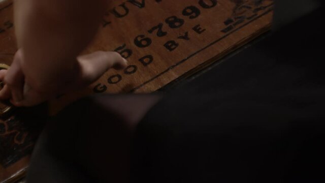 Hands Moving Planchette Over Ouija Board And Spelling Azazel