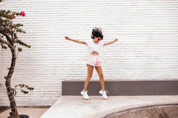 Full length view of pleased girl jumping on street. Outdoor shot of charming tanned woman in shorts.