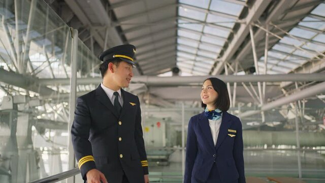 Asian pilot and flight attendant talking while walking in the airport.