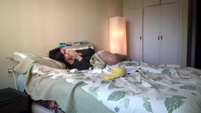 Latin American girl coughing and sneezing lying on a bed