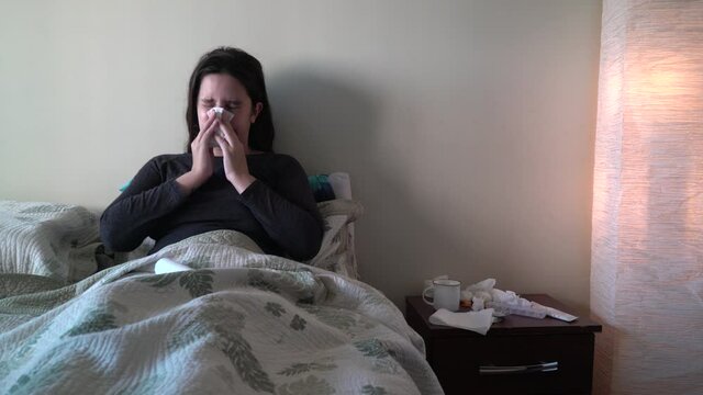 Young woman with a cold wiping her nose sitting on bed